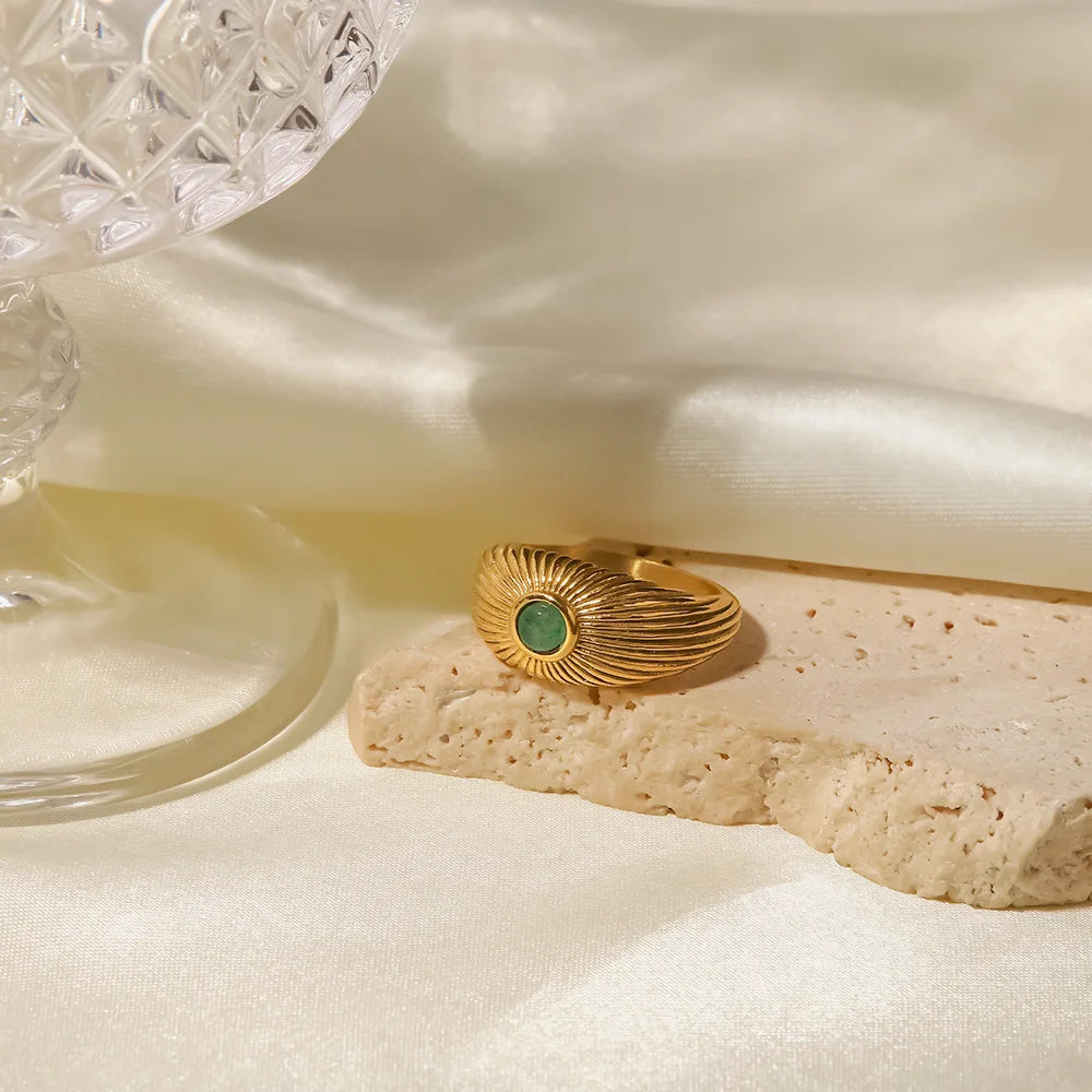 Green Stone Geometric Wrap Ring beautifully displayed on a textured stone surface next to a crystal glass.